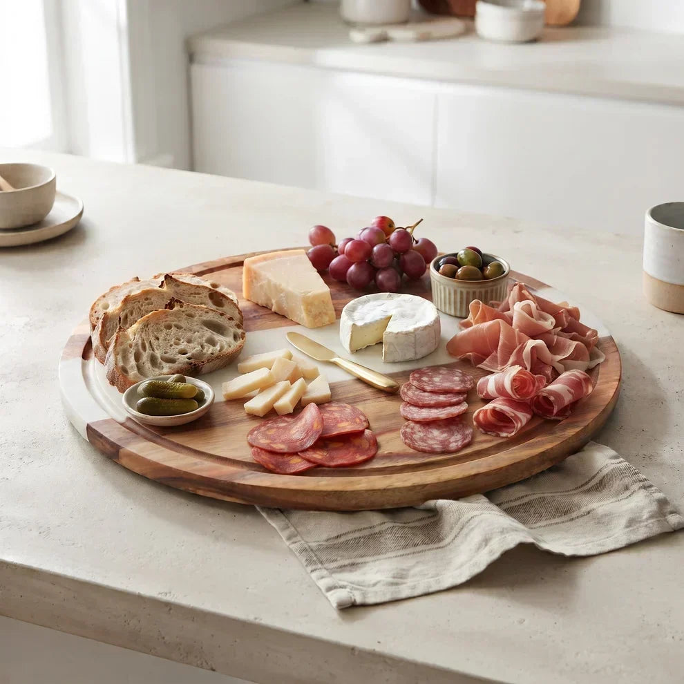 Creative Gifts charcuterie board with cheese, meats, grapes, bread, and olives on a kitchen table.