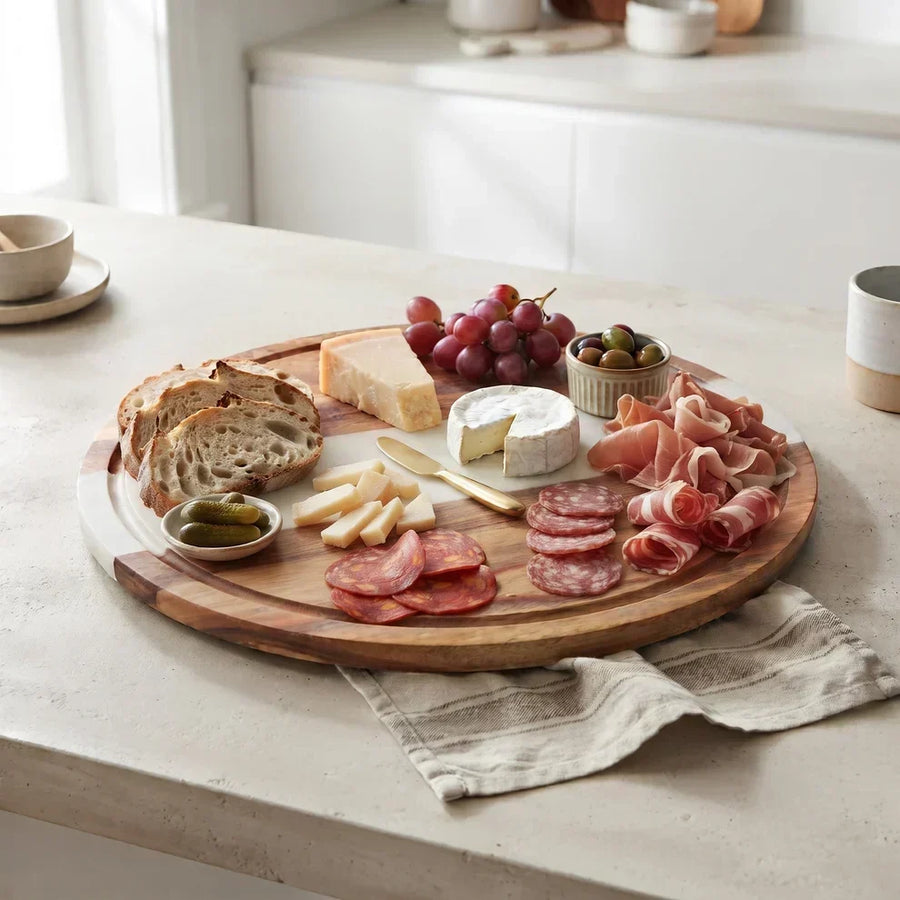 Creative Gifts charcuterie board with cheese, meats, grapes, bread, and olives on a kitchen table.