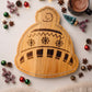 Winter hat-shaped wood serving board, 13.5 x 15 inches, with festive stripes, snowflake details, and pompom accent for serving snacks and appetizers.
