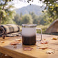 White and black 12 oz stainless steel travel mug with handle, vacuum insulation, and leak-proof push-pull lid for hot or cold drinks on the go.
