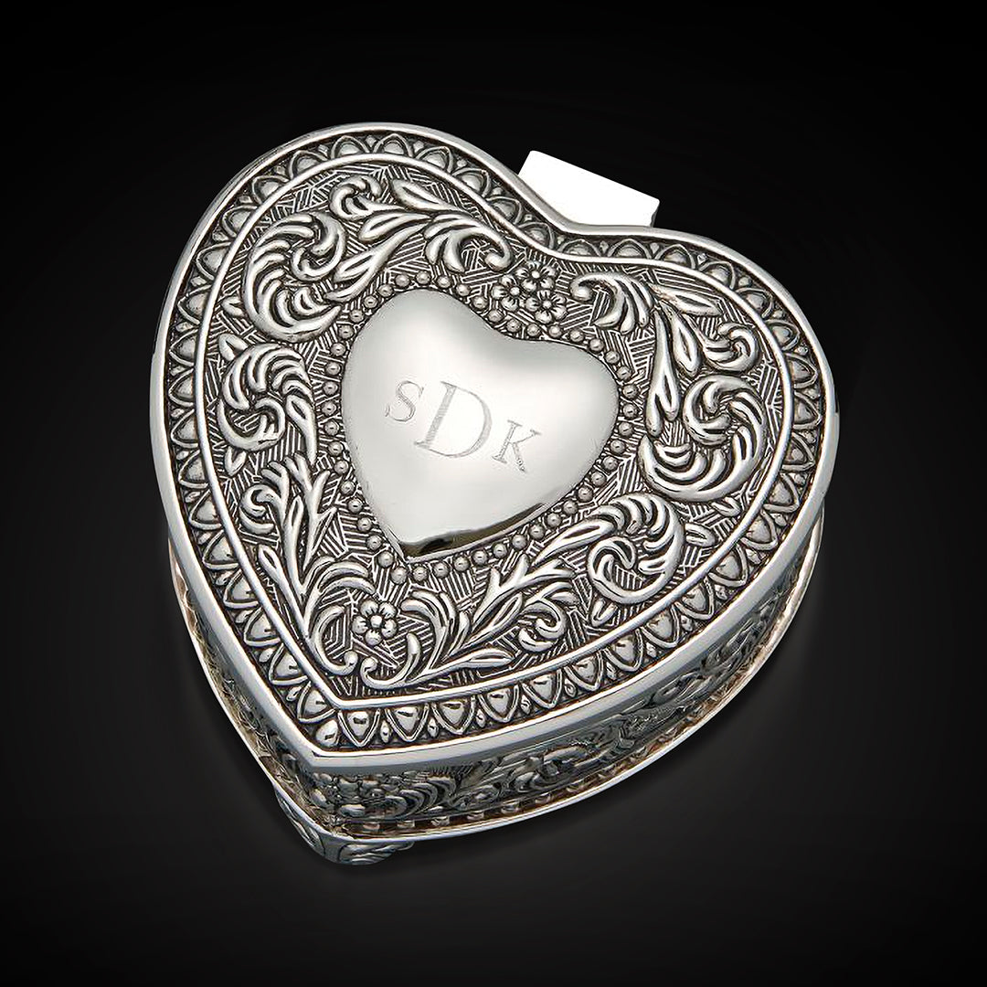 A personalized heart-shaped silver keepsake box with elaborate scrollwork and the engraved initials "SDK" on the lid.