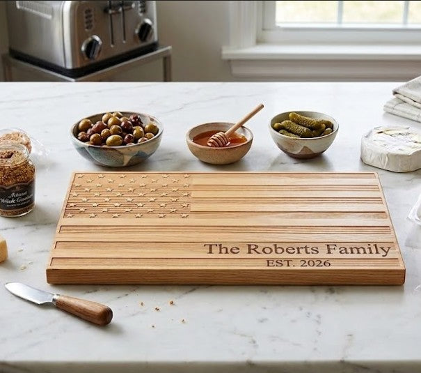 Engraved American Flag-shaped acacia wood serving board in a natural brown finish, designed for charcuterie, cheese, fruit, or appetizers, and suitable for personalization as a unique gift.