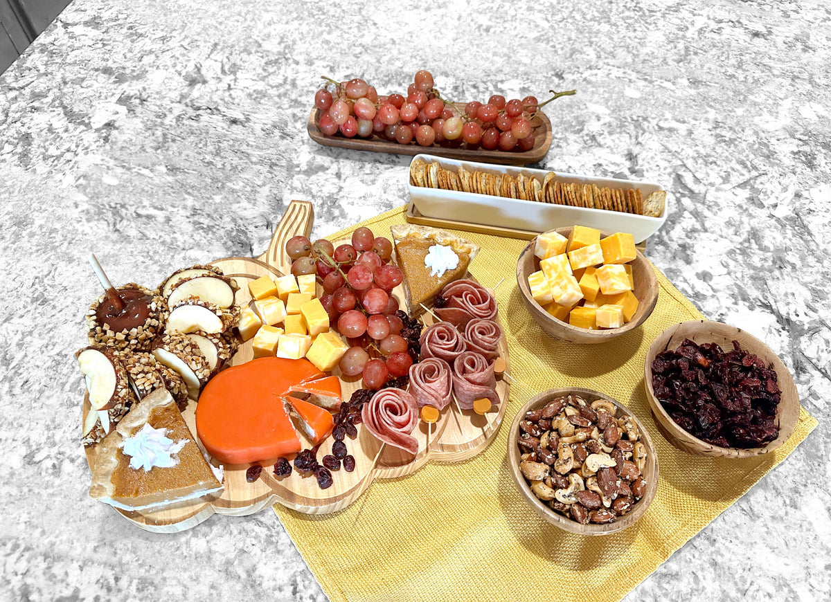 A personalized wooden pumpkin-shaped charcuterie board with cheeses, grapes, meats, candied apples, nuts, and crackers.